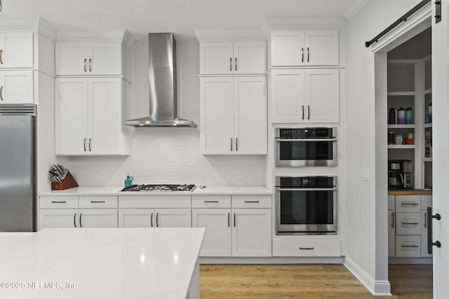 kitchen featuring white cabinetry, appliances with stainless steel finishes, a barn door, and wall chimney range hood