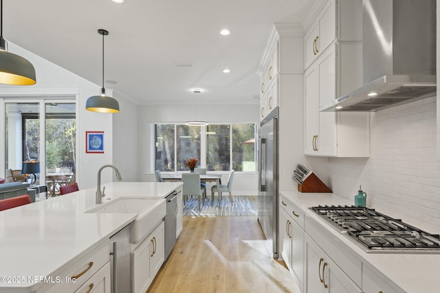 kitchen featuring sink, appliances with stainless steel finishes, white cabinetry, decorative light fixtures, and wall chimney exhaust hood