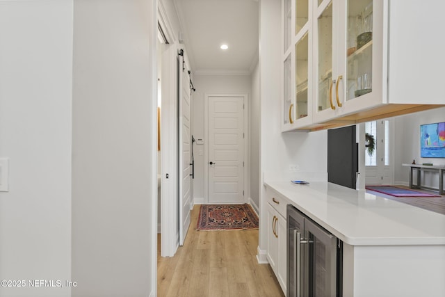 interior space with white cabinets, beverage cooler, ornamental molding, a barn door, and light wood-type flooring