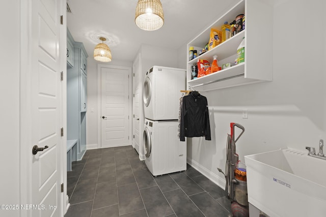 laundry room featuring stacked washer and clothes dryer, sink, and dark tile patterned floors