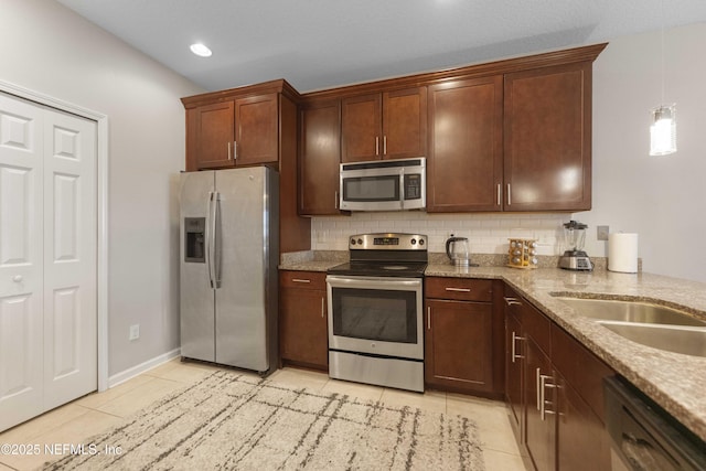 kitchen with appliances with stainless steel finishes, decorative light fixtures, light tile patterned floors, light stone counters, and decorative backsplash