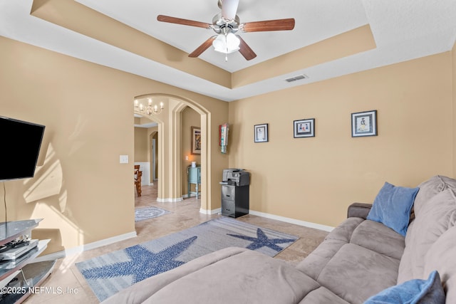 living room featuring ceiling fan with notable chandelier and a tray ceiling