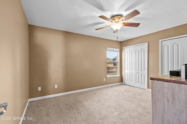 unfurnished bedroom with multiple closets, ceiling fan, light carpet, and a textured ceiling