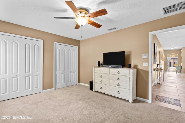 bedroom featuring a textured ceiling, ceiling fan with notable chandelier, light colored carpet, and multiple closets