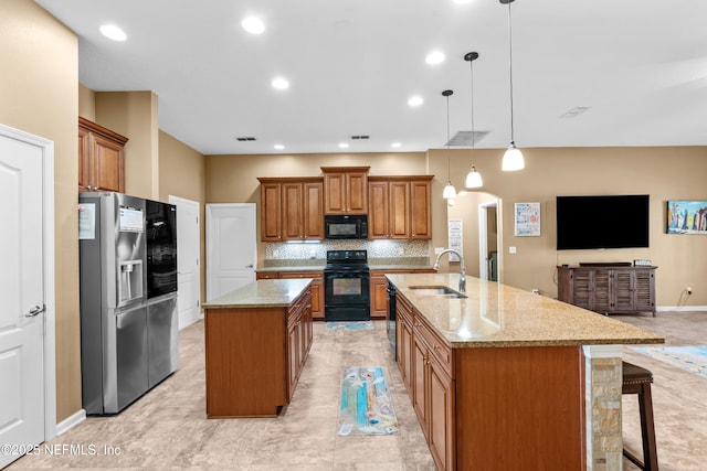 kitchen with a spacious island, a kitchen bar, light stone counters, pendant lighting, and black appliances