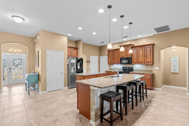 kitchen with sink, light stone counters, a kitchen breakfast bar, a kitchen island with sink, and black appliances