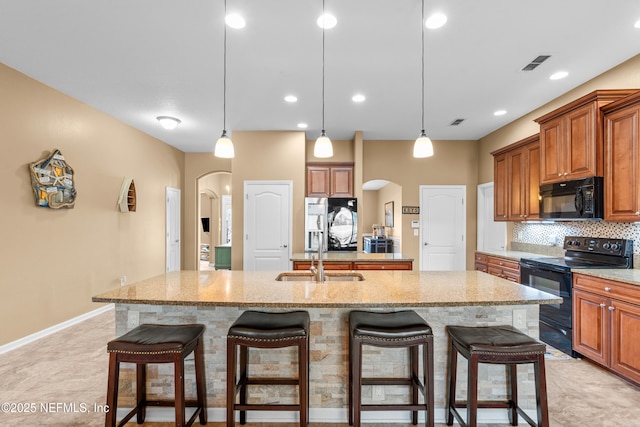 kitchen featuring a kitchen bar, sink, a kitchen island with sink, decorative backsplash, and black appliances