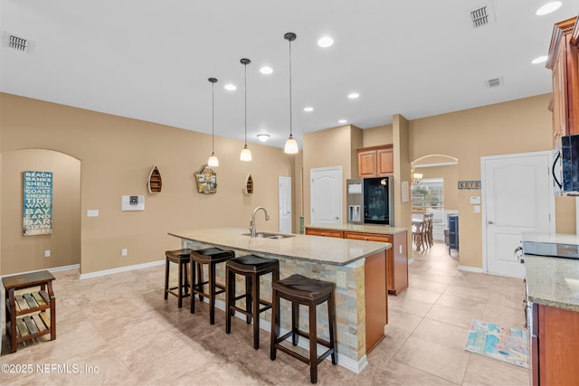 kitchen featuring pendant lighting, sink, light stone counters, an island with sink, and stainless steel fridge with ice dispenser