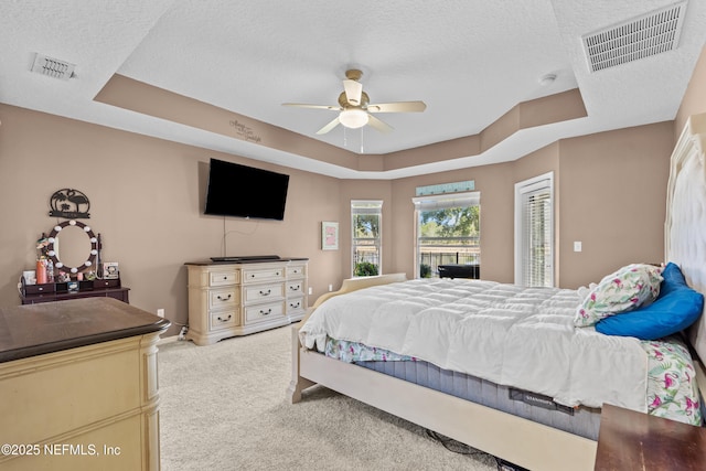 bedroom with ceiling fan, light colored carpet, a textured ceiling, and a tray ceiling