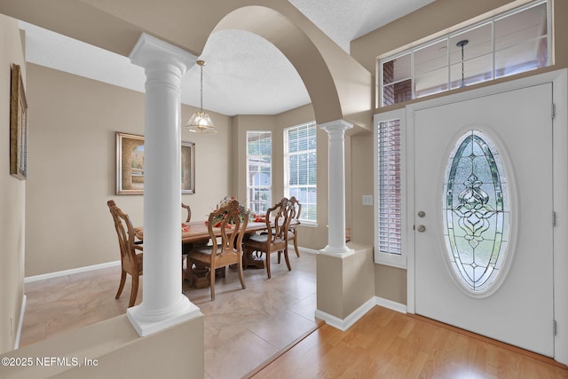 entrance foyer featuring light hardwood / wood-style floors, a textured ceiling, and ornate columns