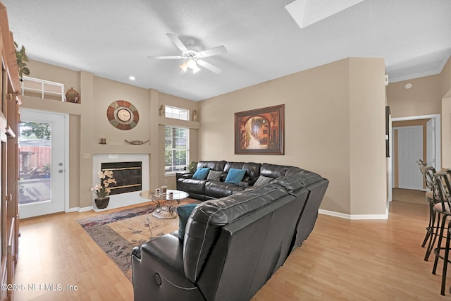 living room featuring ceiling fan, a textured ceiling, light hardwood / wood-style floors, and a skylight