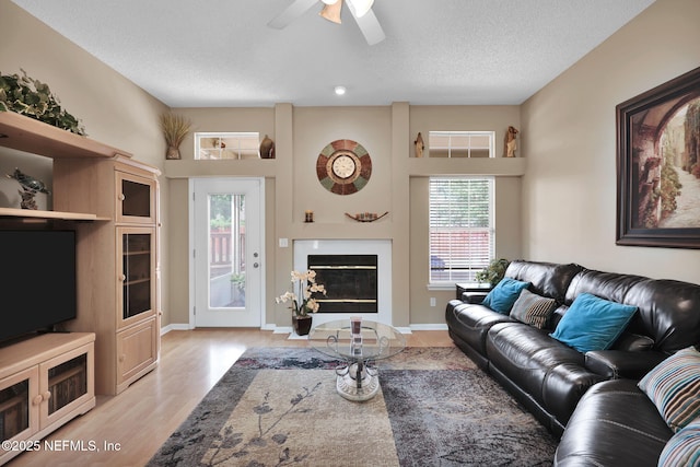 living room with ceiling fan, a textured ceiling, and light wood-type flooring