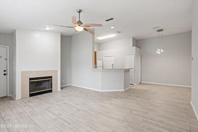 unfurnished living room with a tiled fireplace, ceiling fan, light wood-type flooring, and a textured ceiling