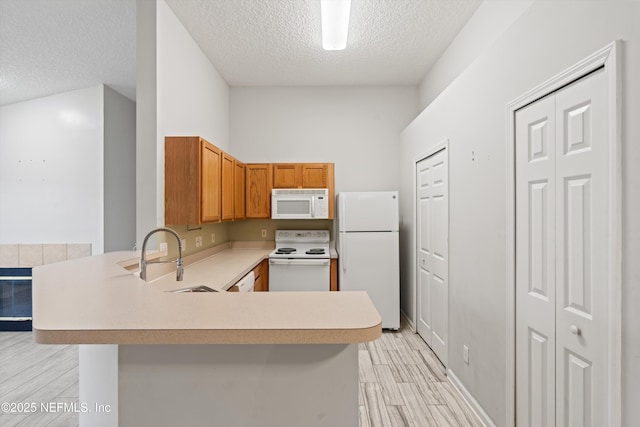 kitchen with sink, white appliances, light hardwood / wood-style floors, a textured ceiling, and kitchen peninsula