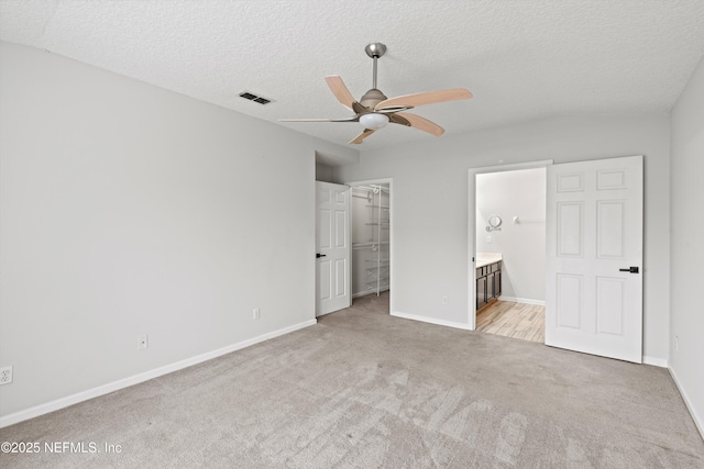 unfurnished bedroom featuring ceiling fan, ensuite bathroom, light carpet, a spacious closet, and a closet