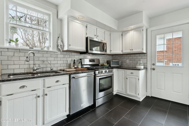 kitchen with sink, appliances with stainless steel finishes, white cabinetry, dark tile patterned flooring, and decorative backsplash