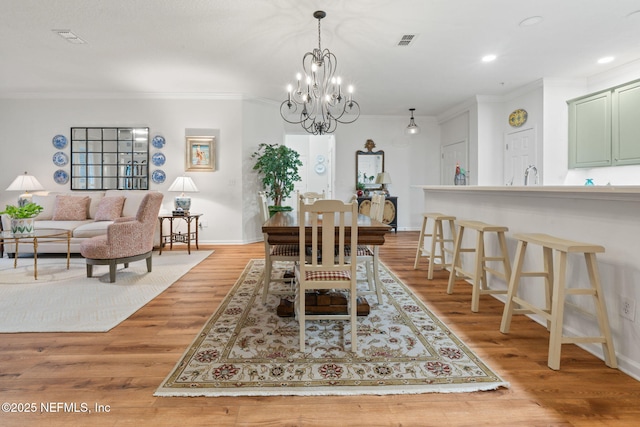 dining area with crown molding, a notable chandelier, sink, and light wood-type flooring