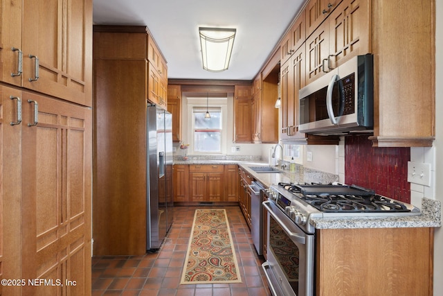 kitchen with light stone countertops, dark tile patterned flooring, appliances with stainless steel finishes, decorative backsplash, and sink