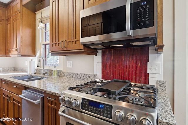 kitchen featuring sink, decorative light fixtures, light stone countertops, and stainless steel appliances