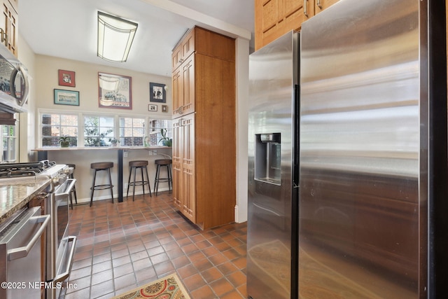 kitchen featuring stainless steel appliances, light stone countertops, dark tile patterned flooring, and a kitchen breakfast bar