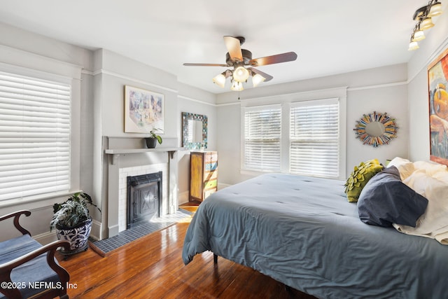 bedroom with wood-type flooring, a fireplace, and ceiling fan