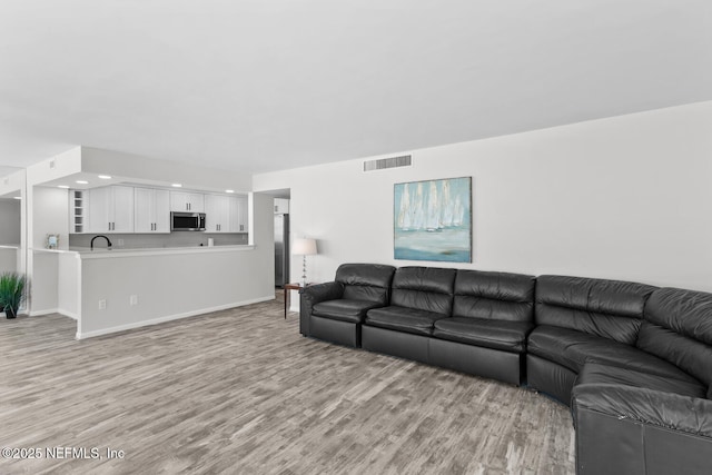 living room featuring light wood-type flooring, visible vents, and baseboards