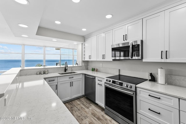 kitchen featuring light stone counters, a sink, white cabinetry, light wood-style floors, and appliances with stainless steel finishes