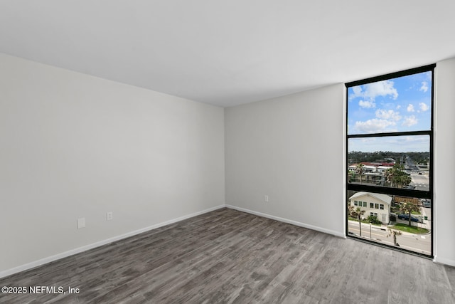 spare room featuring baseboards, wood finished floors, and floor to ceiling windows