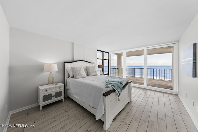 bedroom featuring a wall of windows, access to outside, a water view, and light wood-style floors