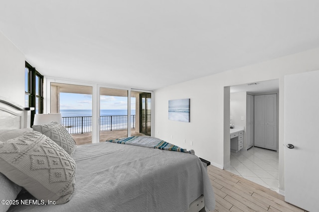 bedroom featuring a water view, baseboards, access to outside, light wood-type flooring, and expansive windows