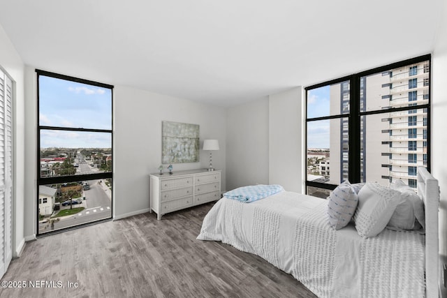 bedroom with expansive windows, wood finished floors, and baseboards