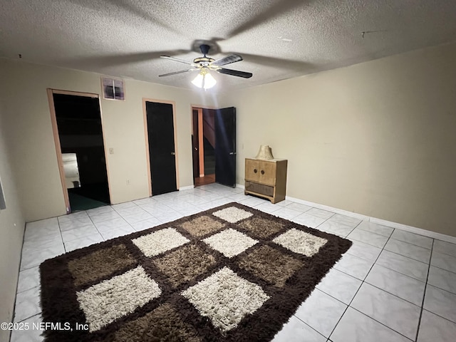 unfurnished bedroom with a textured ceiling, light tile patterned floors, ceiling fan, and a walk in closet