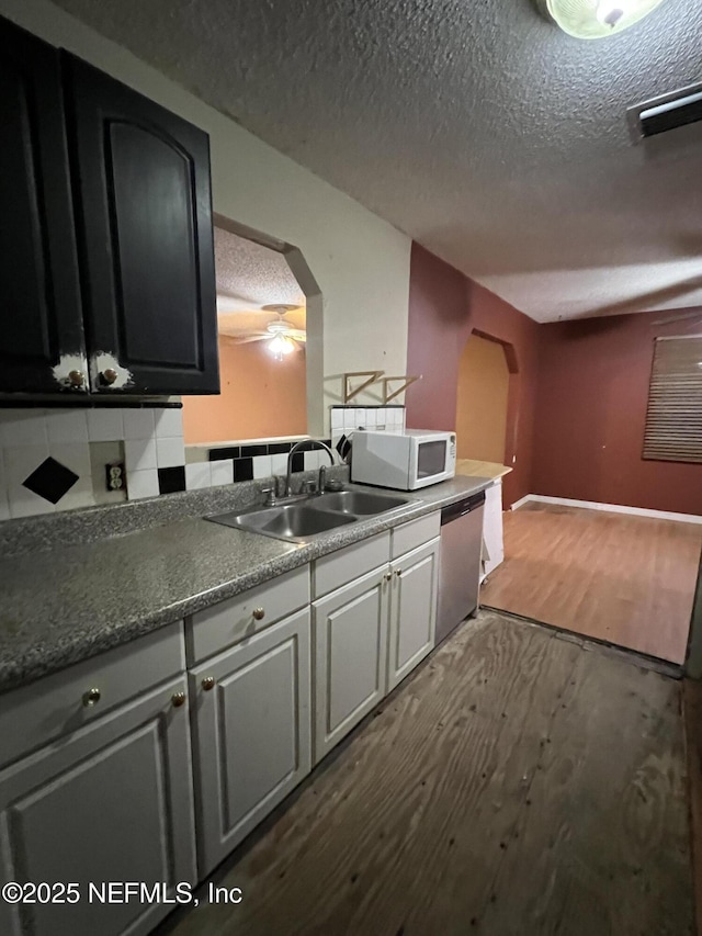 kitchen featuring a textured ceiling, decorative backsplash, stainless steel dishwasher, sink, and dark wood-type flooring