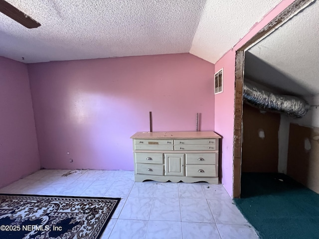 unfurnished bedroom featuring light tile patterned floors, a textured ceiling, vaulted ceiling, and ceiling fan