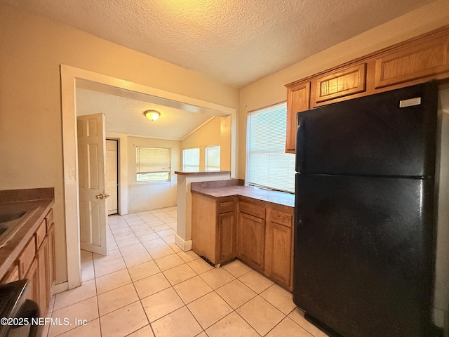 kitchen with black refrigerator, a textured ceiling, lofted ceiling, and light tile patterned flooring