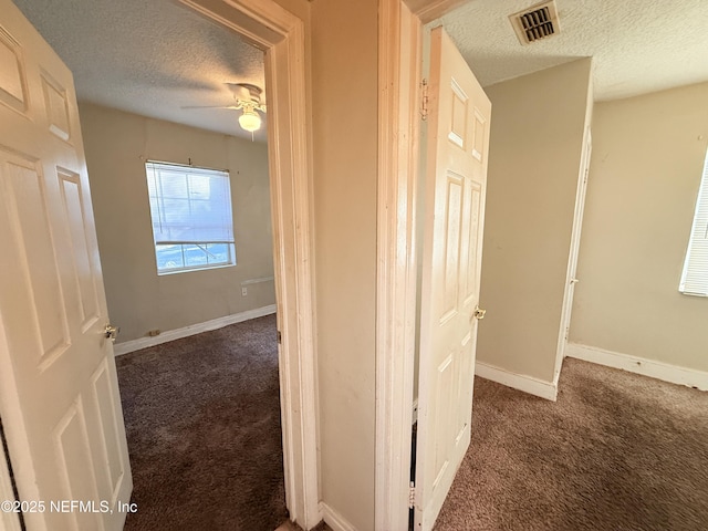 hall featuring a textured ceiling and dark carpet