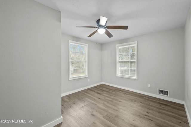 spare room with ceiling fan, plenty of natural light, and wood-type flooring