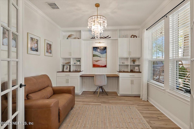 office featuring a notable chandelier, ornamental molding, built in desk, and light wood-type flooring