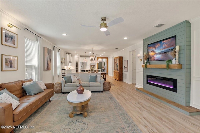 living room featuring ceiling fan with notable chandelier, light hardwood / wood-style flooring, ornamental molding, and a textured ceiling