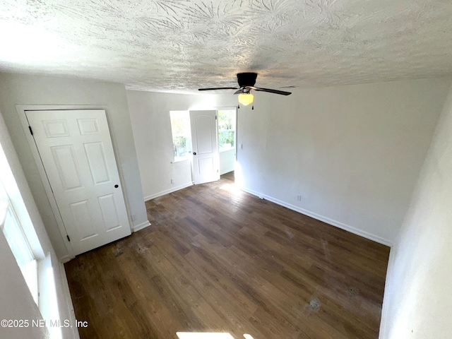 empty room with ceiling fan, dark wood-type flooring, and a textured ceiling