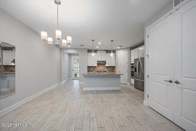 kitchen featuring appliances with stainless steel finishes, pendant lighting, white cabinets, a kitchen island with sink, and light hardwood / wood-style flooring