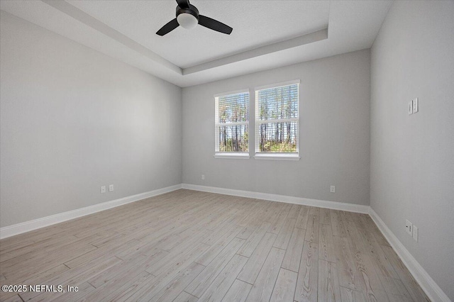 empty room featuring ceiling fan, a tray ceiling, and light hardwood / wood-style flooring