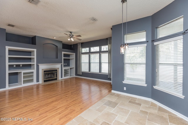 unfurnished living room featuring built in features, a healthy amount of sunlight, and a textured ceiling