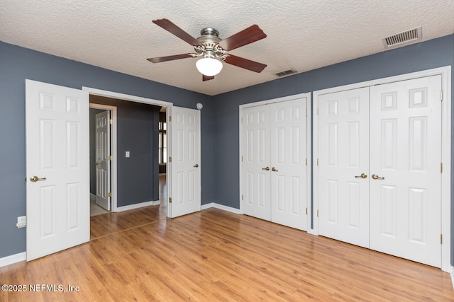 unfurnished bedroom with ceiling fan, two closets, light hardwood / wood-style flooring, and a textured ceiling