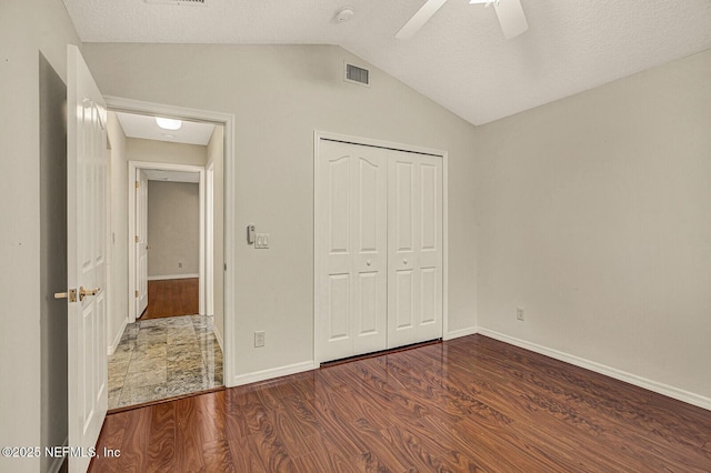 unfurnished bedroom with ceiling fan, a textured ceiling, dark hardwood / wood-style flooring, vaulted ceiling, and a closet