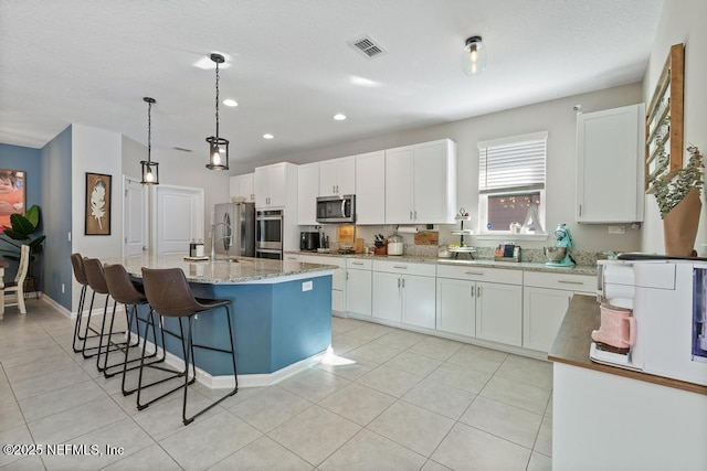 kitchen featuring hanging light fixtures, white cabinets, light stone countertops, an island with sink, and stainless steel appliances