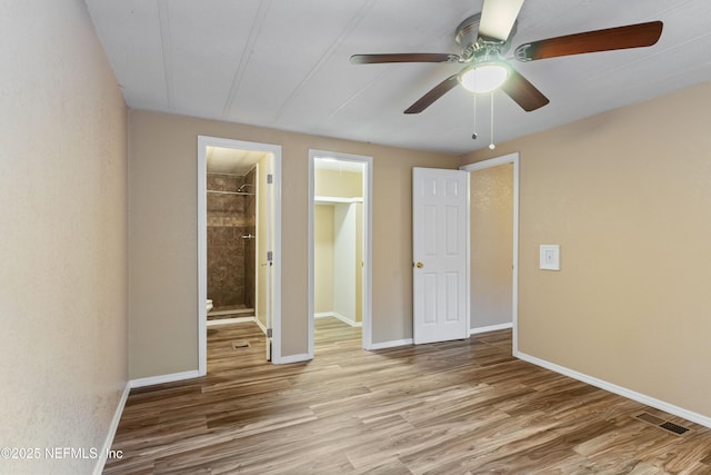 unfurnished bedroom with light wood-type flooring, ensuite bath, ceiling fan, and a walk in closet