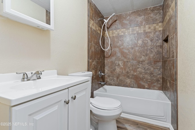 full bathroom with a textured ceiling, tiled shower / bath combo, vanity, toilet, and hardwood / wood-style flooring