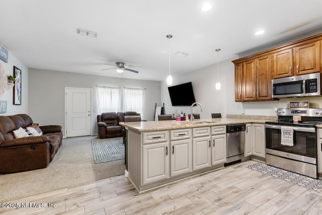 kitchen with light stone countertops, stainless steel appliances, sink, hanging light fixtures, and kitchen peninsula