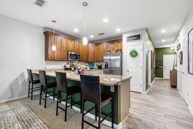 kitchen featuring a kitchen breakfast bar, kitchen peninsula, appliances with stainless steel finishes, decorative light fixtures, and light stone counters